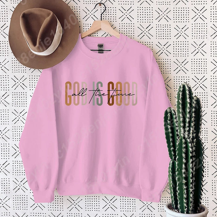 Pink Christian clothing women sweatshirt with God is Good design hanging on wall with brown hat and cactus