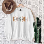 White sweatshirt with God is Good call the fence design, styled with brown hat and cactus, Christian clothing women