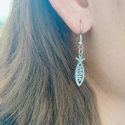 Silver Christian fish earrings with Jesus inscription worn on ear showing detailed design