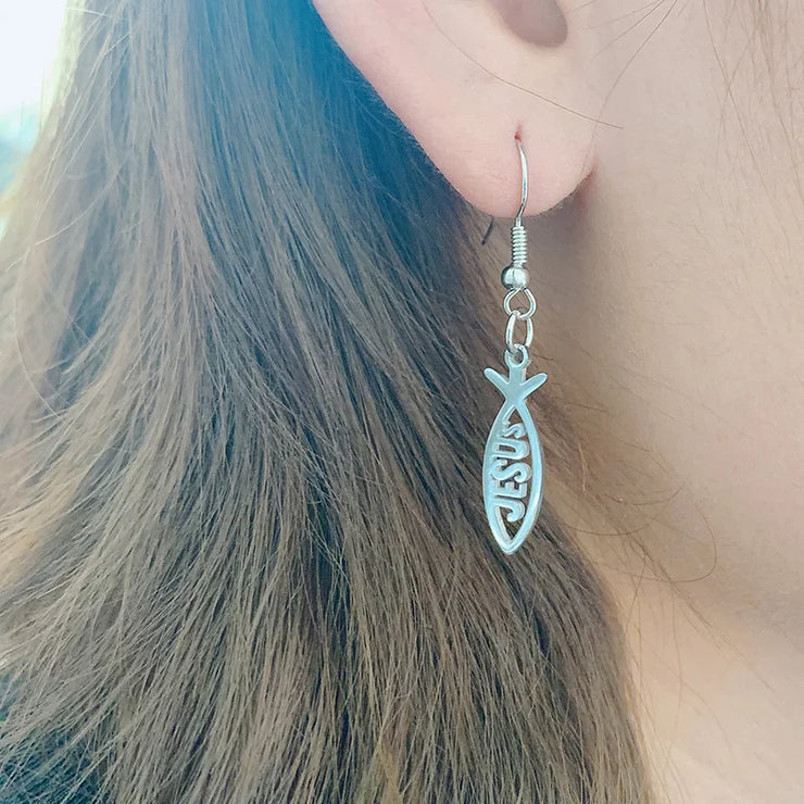 Silver Christian fish earrings with Jesus inscription worn on ear showing detailed design