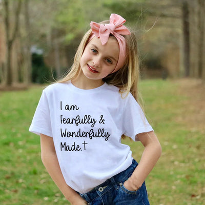Young girl wearing a white Christian kids t-shirt with I am fearfully and wonderfully made text outdoors