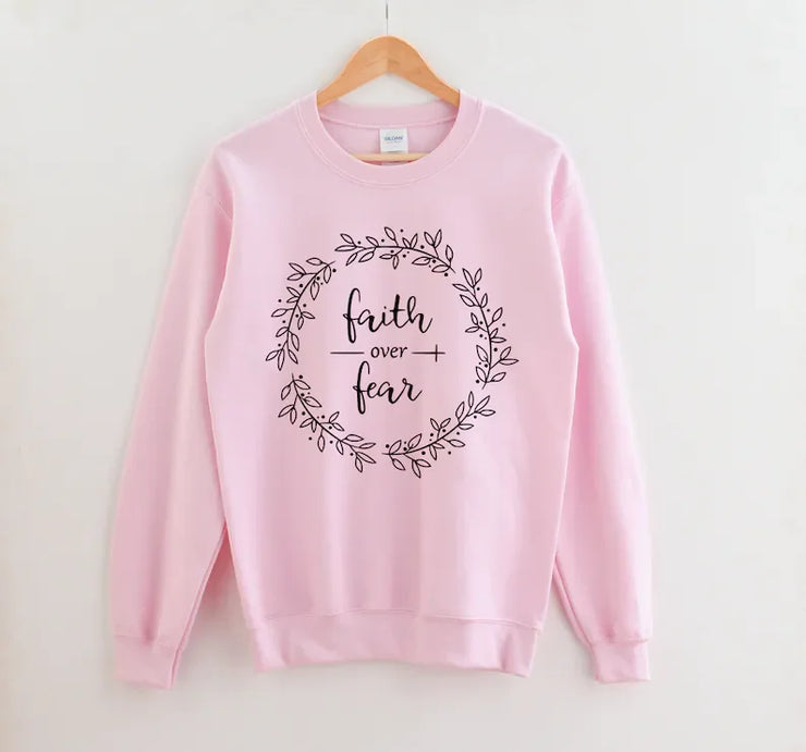 Pink Christian women's sweatshirt with faith over fear floral wreath design hanging on wooden hanger