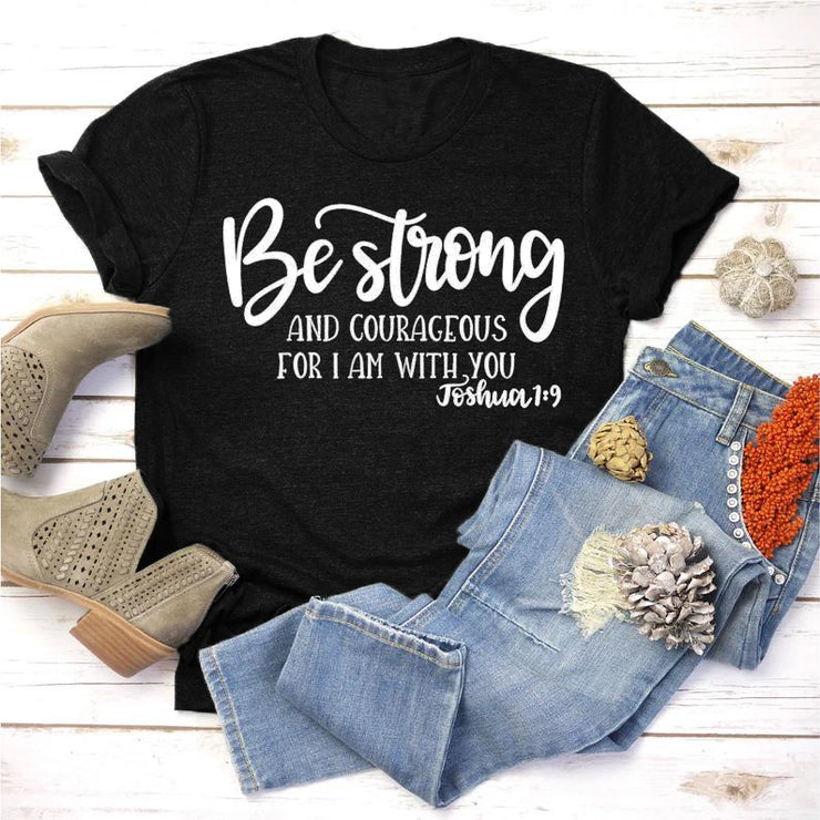Black faith based apparel t-shirt with Be Strong Joshua 1:9 scripture paired with blue jeans and beige boots