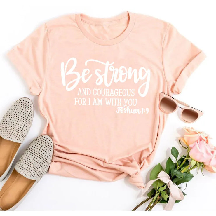 Peach t-shirt with Be Strong Joshua 1:9 scripture design paired with sunglasses and shoes Faith Based Apparel