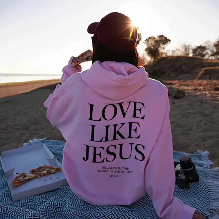 Person wearing pink Faith based apparel hoodie with Love Like Jesus design sitting on beach with pizza