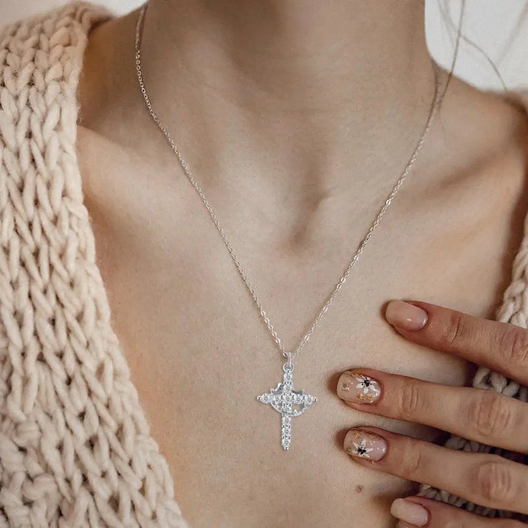 Elegant silver faith-based cross necklace worn on a delicate chain with floral nail art and a cozy knit sweater