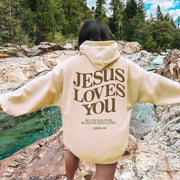 Cream faith-based hoodies with Jesus Loves You biblical quote worn outdoors by creek