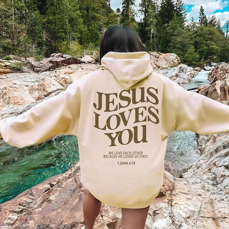 Cream faith-based hoodies with Jesus Loves You biblical quote worn outdoors by creek