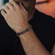 Braided leather bracelet with black cross charm worn on wrist faith jewelry for men