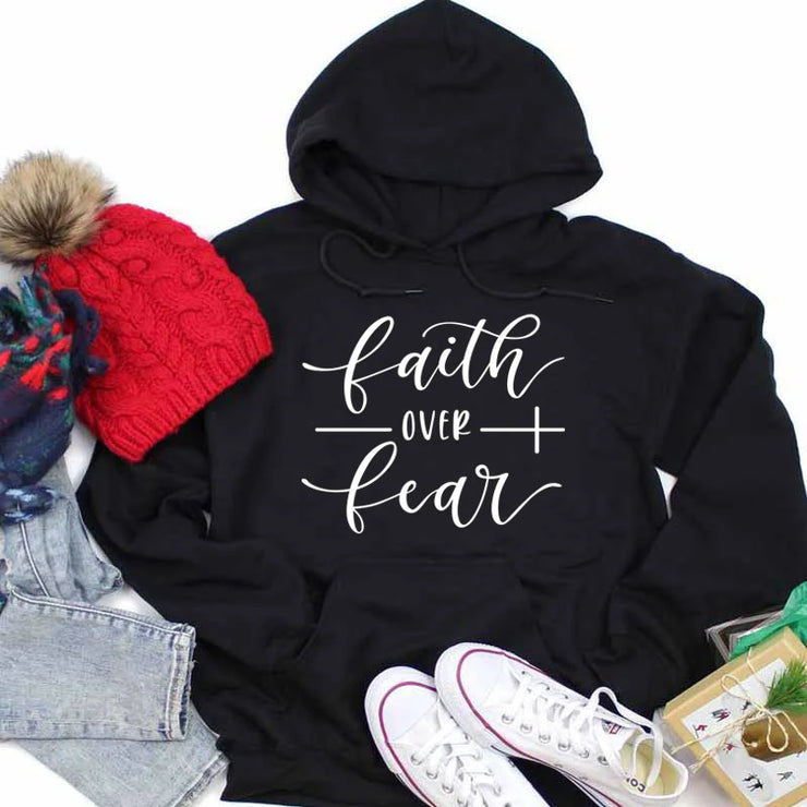 Black hoodie with faith over fear text in white, styled with red knit hat, jeans, and white sneakers religious casual apparel