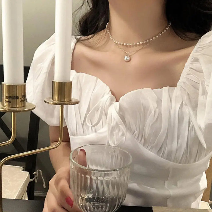 Fresh Faith Designs fashion crystal cross necklace worn with layered pearl and pendant chains on woman in white dress